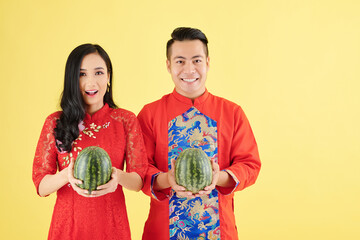 Poster - Portrait of happy young Asian couple in traditional Lunar New Year costumes holding fresh ripe watermelons