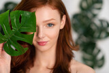 Fototapeta  - Red-Haired Young Woman Posing With Tropical Leaf Over White Background