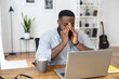 © Vadim Pastuh - Desperate young African-American business entrepreneur in smart casual attire, touching the face, feeling stressed and overwhelmed while sitting in the office with an open laptop and a cup of coffee