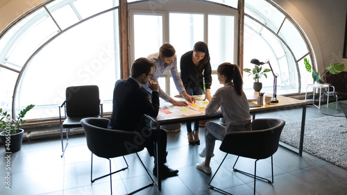 Fototapeta na szkło Diverse employees working with project documents, using sticky papers, writing notes, colleagues developing business project strategy, marketing plan, analyzing charts and diagrams in modern office