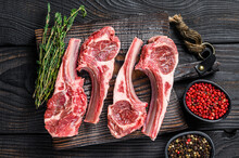 Lamb Chops Raw Meat On Bone With Salt, Pepper And Herbs. Black Wooden Background. Top View