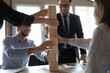 © fizkes - Close up happy diverse employees involved in team building activity at meeting, motivated colleagues playing with wooden cubes, building tower, staff training, teamwork and collaboration concept