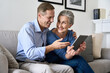 © insta_photos - Happy older mature couple using digital tablet sitting on sofa at home. Smiling senior retired family 60s husband and wife holding pad enjoying modern technology shopping or banking online together.