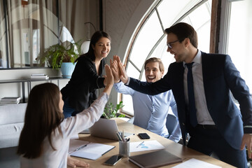 Wall Mural - Excited diverse colleagues giving high five, showing unity at meeting, celebrating business success, achievement, coworkers engaged in team building activity, teamwork, collaboration concept