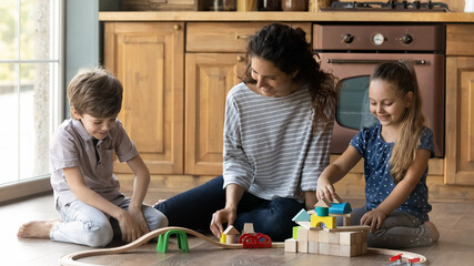 Wall Mural - Wide banner panorama view of happy mom have fun playing toys with little children at home. Smiling young Caucasian mother and small kids engaged in funny game activity feel playful in cozy kitchen.