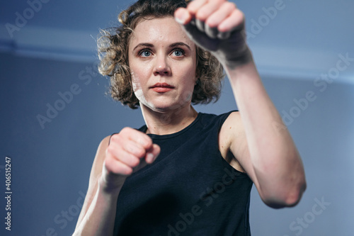 Female fighter throws punches directly into camera. Woman athlete taekwondo strikes sharp, quick strikes, looking directly into camera, quick movements against wall. Self defense concept for women