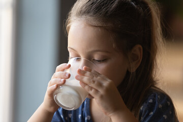 Close up of cute little Caucasian 6s girl kid drink tasty organic wholegrain milk with vitamins calcium from glass. Small child enjoy delicious nutritious lactose free yoghurt. Healthcare concept.