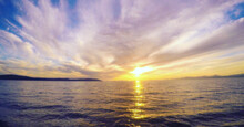 Wavy Ocean Gleaming Under The Sunset Piercing Through The Clouds - Great For Wallpapers