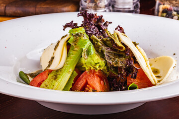 Wall Mural - Italian caprese salad with sliced tomatoes, mozzarella cheese, pesto sauce, lettuce on white plate.