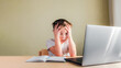 © OlgaKhorkova - Desperate Child sits at a desk, looks sadly at the computer and holds his head with his hands. Online learning problem concept