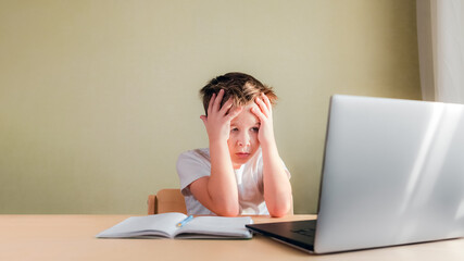 Desperate Child sits at a desk, looks sadly at the computer and holds his head with his hands. Online learning problem concept