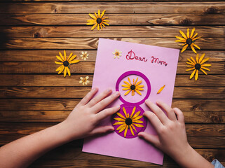 Dear mom written on a piece of paper with dried flowers. Children's hands make a postcard to mom in honor of the 8 March holiday. Children's creativity, handmade. Ikebana, wooden background.