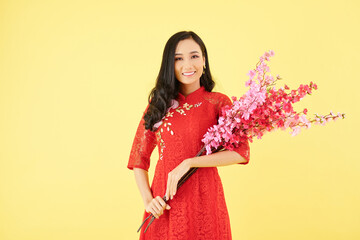 Poster - Portrait of young beautiful smiling Asian woman holding bouquet of blooming peach branches