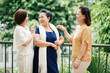© DragonImages - Group of senior Vietnamese female friends standing on balcony, discussing news and joking around