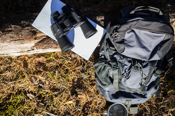 Wall Mural - Tourist backpack, hat, binoculars and a map on a log in the forest. Concept of hiking, hiking in the mountains. Banner. Top view