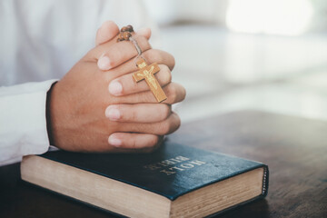 Man praying, hands clasped together on her Bible.
