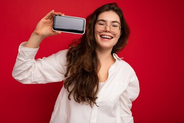 Photo of beautiful smiling young woman good looking wearing casual stylish outfit standing isolated on background with copy space holding smartphone showing phone in hand with empty screen display for