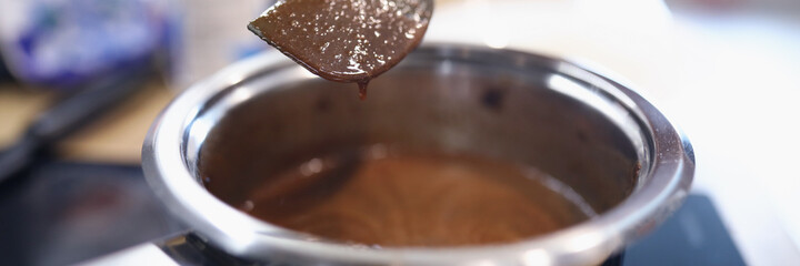 Ladle of sauce is on electric stove. Female hand hold spoon close up and mix cream in kitchen.