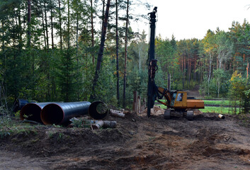 Poster - Vibrating hydraulic hammer in forest area. Hydraulically driven free-fall hammer for impact driving of steel pipes. Laying pipes underground through the railroad. Piling for deep foundation