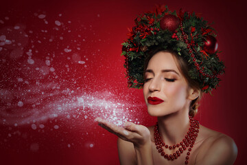 Canvas Print - Beautiful young woman with Christmas wreath blowing kiss on red background