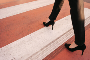 Close up woman legs in black pants and high hills shoes walking on zebra