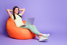 Photo Portrait Full Body View Of Girl Relaxing With Laptop Hands Behind Head In Bean Bag Chair Isolated On Vivid Violet Colored Background