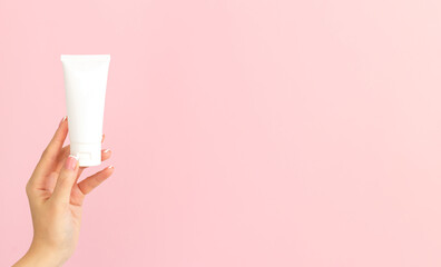 Female hand holding blank white cosmetic tube on pink background