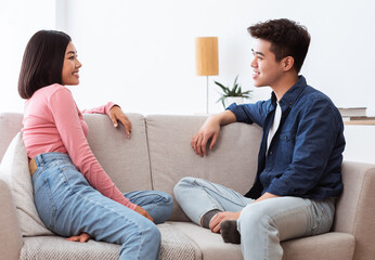 Wall Mural - Lovely Asian Couple Talking Enjoying Flirt Sitting On Sofa Indoor