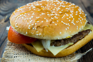 Close-up of a delicious fresh homemade burger with lettuce, cheese, onions and tomatoes on a wooden table, the concept of a mouth-watering meal