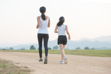 Wall Mural - two female runners jogging outdoors in forest in autumn nature..running sporty mother and daughter. woman and child jogging in a park. outdoor sports and fitness family.