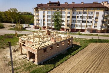 Wall Mural - Aerial view of unfinished brick house with wooden roof frame structure under construction.