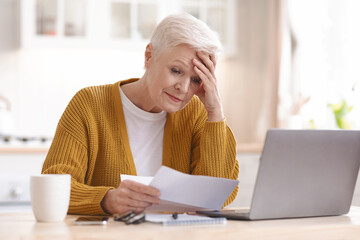 Upset senior lady reading bills, having financial troubles