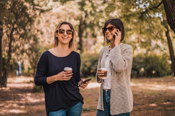 Young women using mobile phones, talking and using app on modern smartphone for browse information strolling with coffee to go