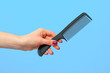© fotofabrika - Female hand holding hair comb against blue background