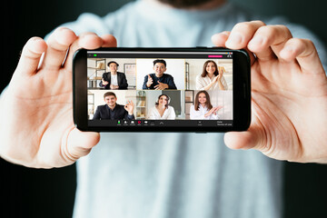 Wall Mural - Video conference. Virtual meeting. Online communication. WFH telework. Man hands showing diverse multiracial team project discussion on mobile app phone screen on blur background.