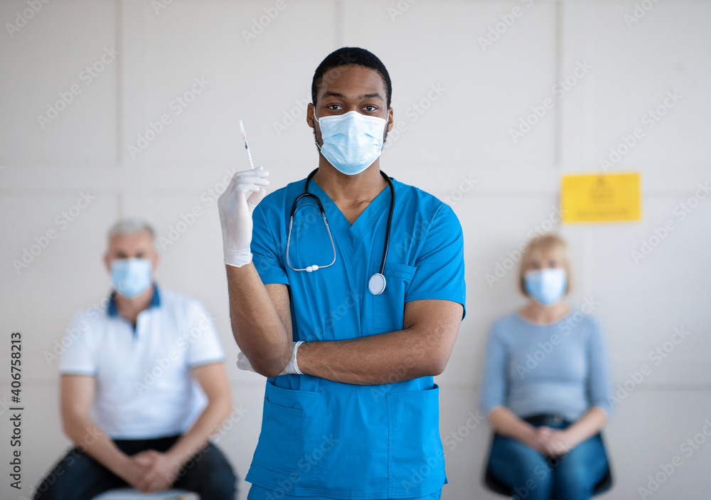 Portrait of young African American doctor in mask and uniform holding syringe with covid-19 vaccine at health centre - obrazy, fototapety, plakaty 
