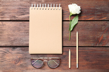 Notebook, eustoma flower, sunglasses and pencils on wooden background, flat lay