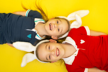 Easter banner with two Cute little girls wearing bunny ears on Easter day. Siblings Girl in bunny ears smiling and looking into camera on yellow background