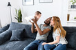 Loving family of three at home sits on the comfortable sofa. Multiracial parents hold biracial newborn baby and look at her with love and care
