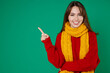 © ViDi Studio - Smiling cheerful young brunette woman 20s in casual knitted red sweater yellow scarf standing pointing index finger aside up on mock up copy space isolated on green color background studio portrait.