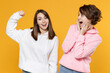 © ViDi Studio - Excited sporty two young women friends 20s wearing casual white pink hoodies standing showing biceps muscles on hand put hand on cheeks isolated on bright yellow color wall background studio portrait.