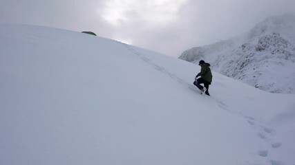 Canvas Print - A man climbing a hill in the mountains through deep snow