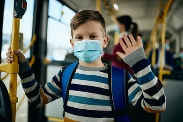 Wall Mural - Happy schoolboy wearing protective face masks while commuting by bus.