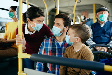 Wall Mural - Happy family with face masks talking while commuting by public transport.