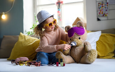 Small girl indoors at home, playing with teddy bear. Lockdown concept.