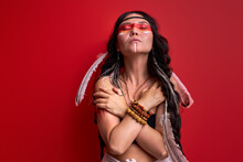 Tribal Woman In Shamanic Clothes Is Shamaning With Closed Eyes, Isolated Over Red Background, Portrait Of Ethnic Woman With Drawings On Body