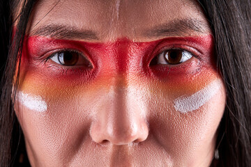 close-up eyes of indian woman confidently looking at camera, serious ethnic female with paintings on face. indian ehnicity, shaman concept