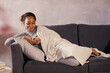 © Сергей Уланов - African girl looks at her phone on the sofa in her cozy room