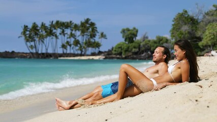 Wall Mural - Vacation travel couple relaxing on beach talking laughing having fun. Happy multiethnic man and woman are lying on sand during summer vacation. They are enjoying on sunny day.