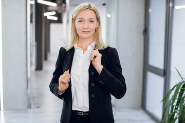 People, business, office, company worker concept. Close up portrait of charming smiling 40 years old lady with blond hair, in formal clothes, posing to camera in front of modern loft light office